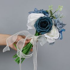 a person holding a bouquet of flowers in their hand on a gray background with white and blue ribbons