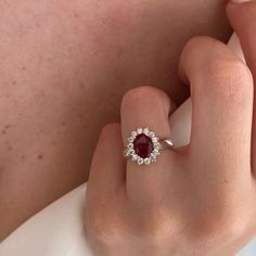 a woman's hand wearing a ring with a red stone surrounded by white diamonds