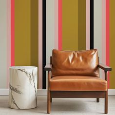 a brown leather chair sitting next to a marble side table in front of a striped wall