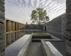 an outdoor courtyard with water and trees in the background, surrounded by stone walls and grass