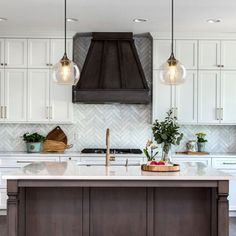 a kitchen with white cabinets and an island in front of the stove, lights hanging from the ceiling