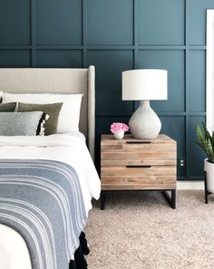 a bed room with a neatly made bed next to a night stand and a potted plant