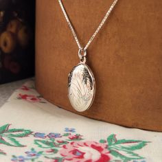 Delicate and timeless, this sterling silver locket is adorned with intricate floral etching, capturing the charm of classic elegance. Perfect for safeguarding cherished memories, it holds two photos and rests gracefully on a slender sterling silver box chain. A thoughtful gift, it arrives with a polishing cloth to maintain its radiant shine. Size: 1" high, 3/8" wide Material: Sterling silver Cheap Silver Locket Jewelry, Cheap Sterling Silver Locket Necklace Gift, Sterling Silver Locket Necklace, Silver Anniversary Gifts, Perfume Jewelry, Clean Sterling Silver, Sterling Silver Locket, Photo Locket Necklace, Silver Locket