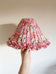 a person holding up a pink lamp shade