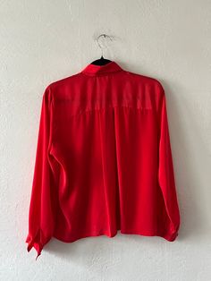 Bright red long sleeve silky collared button up with pleating on the front and a bow at the neckline that is held on with a bobby pin. Unlined with button sleeve cuffs. In excellent vintage condition. DETAILSLabel: Nicole Blake PetitesMaterial: 100% Polyester SIZE & MEASUREMENTSTag Size: 6 Best Fits: XS/Small Length: 24"Bust: 38"Waist: 38"Sleeve: 22"Shoulder: 16" Red Collared Blouse For Fall, Red Long Sleeve Blouse For Evening, Red Party Blouse With Buttons, Red Button-up Party Blouse, Red Button-up Blouse For Party, Red Long Sleeve Blouse For Office, Red Collar Blouse For Work, Red Collared Party Blouse, Red Button-up Blouse For Work