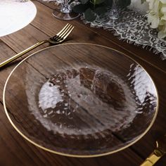 a glass plate on a wooden table with gold rimmed plates and flowers in the background