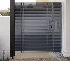 a modern gate is shown in front of a white building with black shutters on it