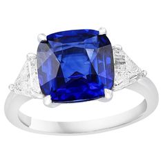 Showcases a Cushion cut, Vibrant color Blue Sapphire weighing 4.09 carats, flanked by two pointed trillion cut diamonds weighing 0.96 carats total. Elegantly set in a polished platinum composition. Classic Cushion Cut Brilliant Gemstones, Formal Trillion Cut Diamond Ring With Gemstone, Gia Certified Trillion Cut Diamond Ring For Formal Occasions, Gia Certified Trillion Cut Diamond Ring For Formal Events, Trillion Cut Diamond Ring With Gemstone For Formal Occasions, Gia Certified Trillion Cut Formal Rings, Formal Gia Certified Trillion Cut Ring, Formal Sapphire Ring With Cushion Diamond Cut, Formal Sapphire Ring With Cushion Cut