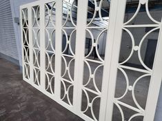 a white metal gate with circular designs on the outside and inside, in front of a building