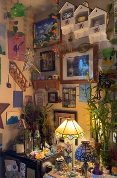 a living room filled with lots of pictures and plants on the wall next to a lamp