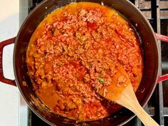 a pan filled with meat and sauce on top of a stove next to a wooden spoon