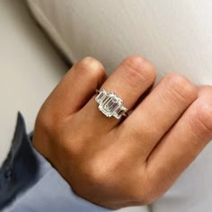 a woman's hand with a diamond ring on top of her finger, resting against a white couch