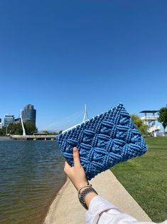 a person is holding up a blue knitted purse over the water's edge