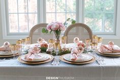 the table is set with pink flowers and gold plates, silverware, and napkins