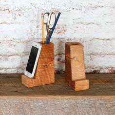 a cell phone, pen and scissors in a holder on a wooden shelf next to a white brick wall