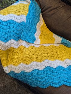 a crocheted blanket sitting on top of a couch next to a brown pillow