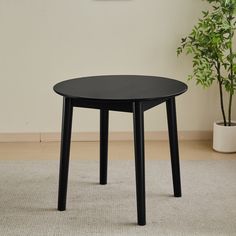 a black table sitting on top of a white rug next to a potted plant