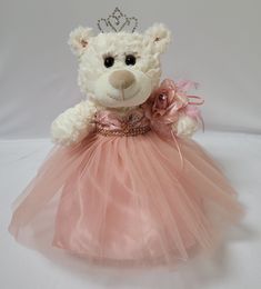 a white teddy bear wearing a pink dress with a tiara on it's head