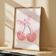 a watercolor painting of two cherries with a pink bow hanging on the wall