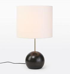 a black lamp with a white shade on it's base and a cord plugged in