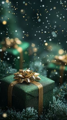 a green present box sitting on top of a christmas tree with gold ribbon and bow