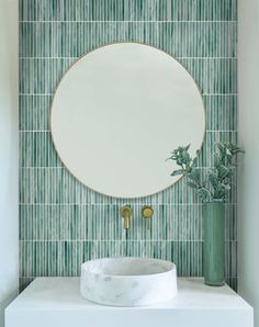 a round mirror sitting on top of a white counter next to a vase with plants