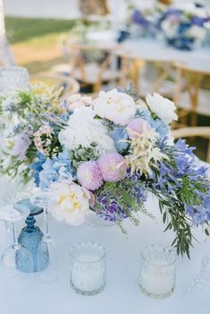 an arrangement of flowers and candles on a white table cloth at a wedding reception in the garden