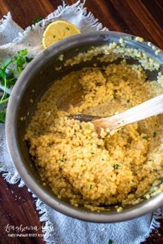 a pot filled with rice and parsley on top of a wooden table next to a lemon wedge