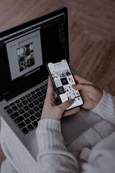 a person sitting in front of a laptop computer holding a cell phone and looking at the screen