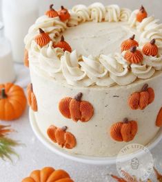 a white cake with orange frosting and pumpkins on it, surrounded by other decorations