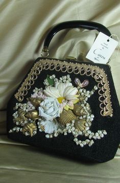 In the handmade/vintage spirit of ETSY, we have Velva Pepper who began decorating handbags and selling them to her friends in the 1950s in Texas. She founded a very successful business. These handbags were all the rage in the 50/60s! This purse was never used, and just the right addition to your summer wardrobe. It would also make an unforgettable gift. The bag is made of a black synthetic fabric. The front is bedazzling with a white daisy, pale blue rose, pink gems, and lots of seashells. Loops Vintage Rectangular Bags For Vintage Events, Vintage Rectangular Bags For Events, Antique Handmade Bags For Vintage Events, Vintage Handmade Bags For Gifts, Retro Handmade Bags For Vintage Fashion, Handmade Antique Bags For Vintage Events, Vintage Satchel Bag As Gift, Handmade Vintage Bag As Gift, Unique Handmade Formal Bag