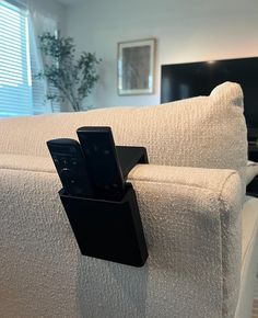 two cell phones are attached to the arm of a couch in front of a tv