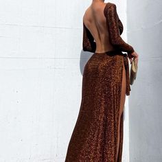 a woman standing next to a white wall wearing a brown and black dress with open back