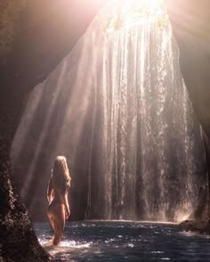 a woman is standing in front of a waterfall with sunlight coming through the water and her body visible