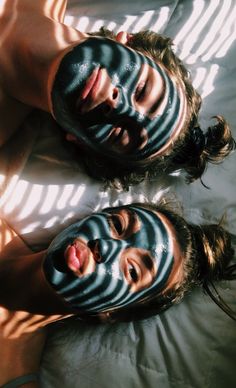 two people with facial masks on their faces laying in the sun, one man has his face painted black and the other is white