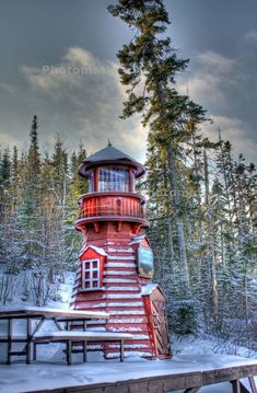 a wooden lighthouse sitting on top of a snow covered ground next to trees and a bridge