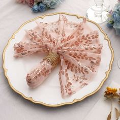 a white plate topped with pink and gold napkins next to flowers on top of a table