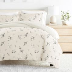 the comforter is made up with white sheets and floral print on it, along with pillows