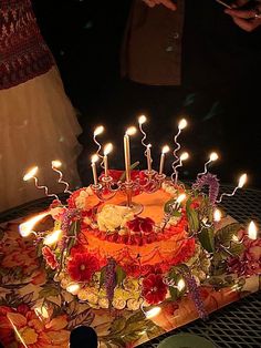 a birthday cake with lit candles on it sitting on a table in front of people