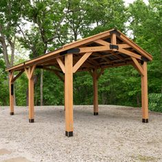 a wooden gazebo sitting on top of a dirt field next to some green trees