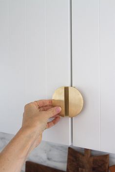 a person is holding the door knob to a cabinet with white cabinets in the background