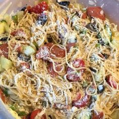 a pasta dish with tomatoes, zucchini and olives in a glass bowl