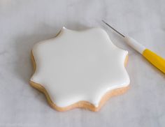 a cookie decorated with white icing next to a pair of yellow handled crochet hooks