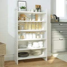 a white book shelf with dishes and plates on it in a clean kitchen, next to a window