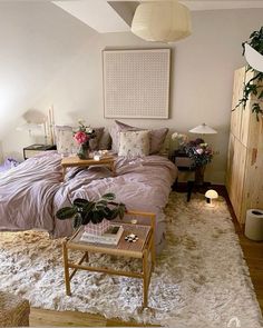 a room with a bed, table and plants in it