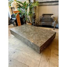 a large square stone coffee table sitting on top of a hard wood floor next to a potted plant