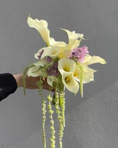 a hand holding a bouquet of flowers on top of a white table next to a gray wall