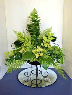 a vase filled with lots of green plants on top of a blue table next to a white wall