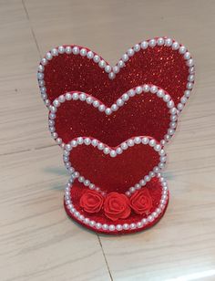 a red heart shaped box with pearls and roses on it's side, sitting on a table