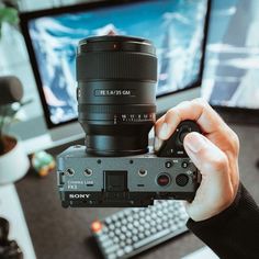 a person holding up a camera in front of a computer